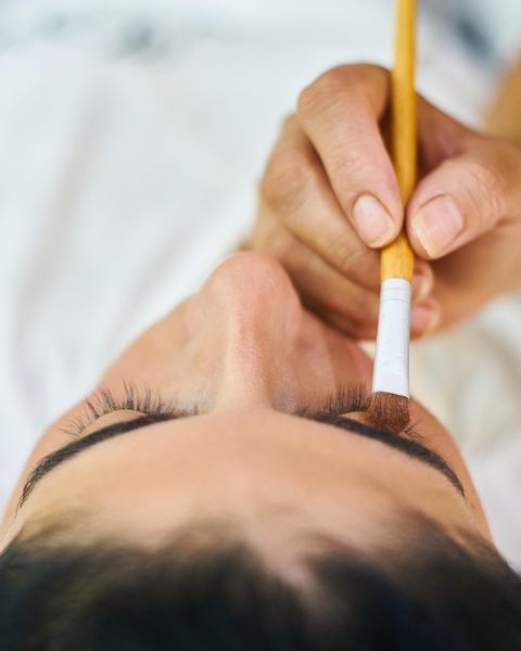 Esthéticienne travaillant le regard d'une cliente allongée, les yeux fermés