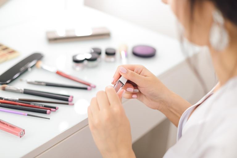 Mains sélectionnant un rouge à lèvres parmi des produits de maquillage